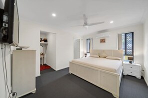 Un dormitorio con una cama grande, un ventilador de techo, un televisor y un escritorio pequeño.