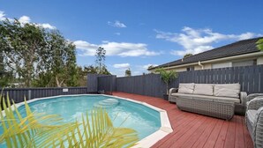 A backyard with a swimming pool, a wooden deck, and outdoor furniture. - Entire 4BR Logan Hidden Gem w/ Pool Near Tamborine (Yarrabilba)