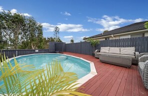 Un patio trasero con piscina, terraza de madera y mobiliario exterior.