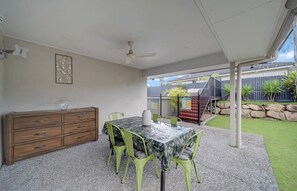 Un espacio al aire libre con patio, una mesa, sillas, un armario de madera y un ventilador de techo.
