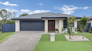 A residential house with a driveway, a garage, a front door, and a small garden with a mailbox. - Entire 4BR Logan Hidden Gem w/ Pool Near Tamborine (Yarrabilba)