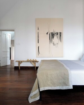 Ein Schlafzimmer mit einem Bett, einer hölzernen Bank und einem großen abstrakten Gemälde an der Wand.