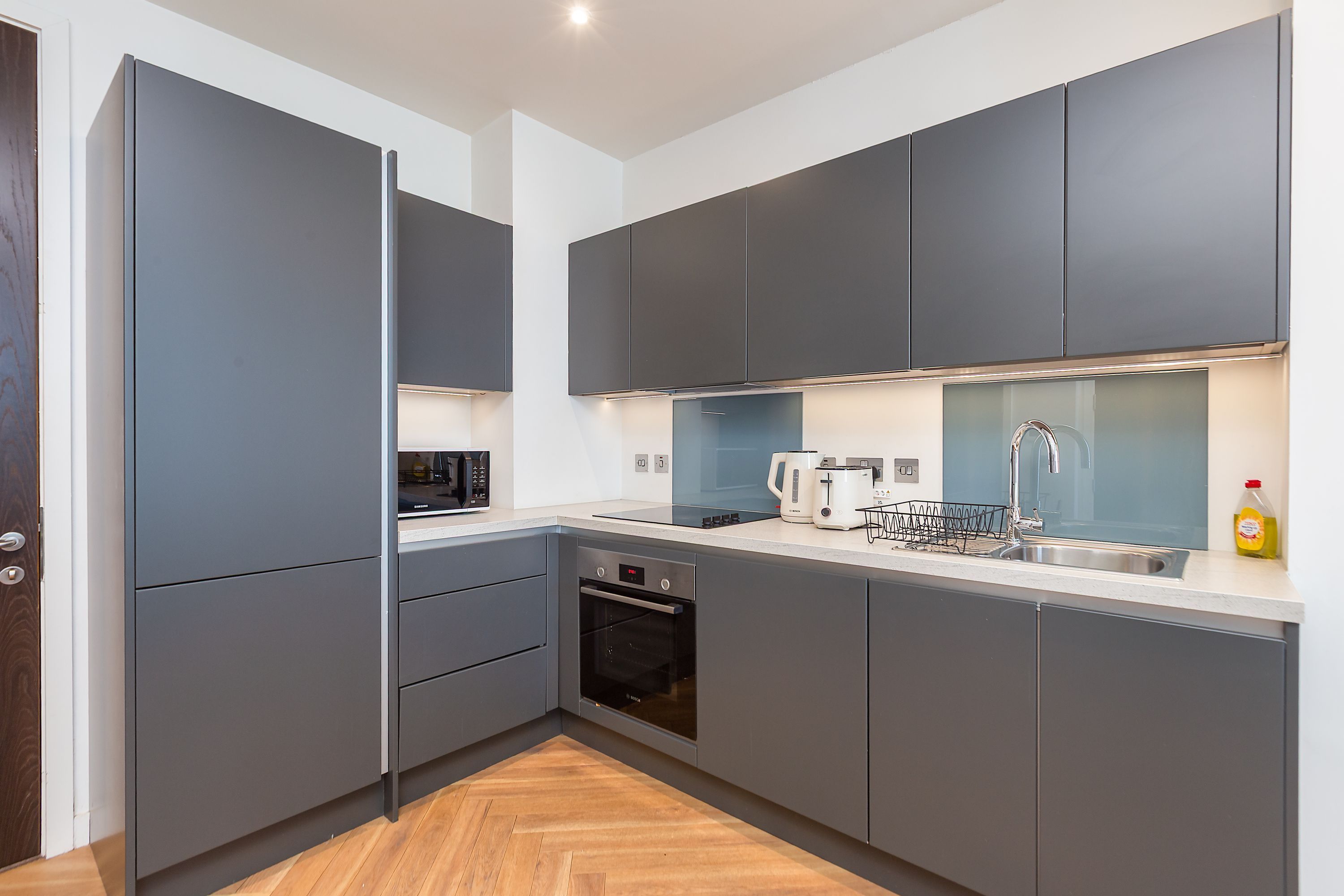 A modern kitchen with grey cabinetry, a built-in oven, and a stainless steel sink.