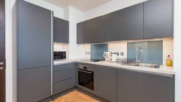 A modern kitchen with grey cabinetry, a built-in oven, and a stainless steel sink.