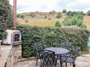 A stone-built outdoor seating area with a brick oven, surrounded by a hedge and overlooking a rural landscape. - South View (Richmond)