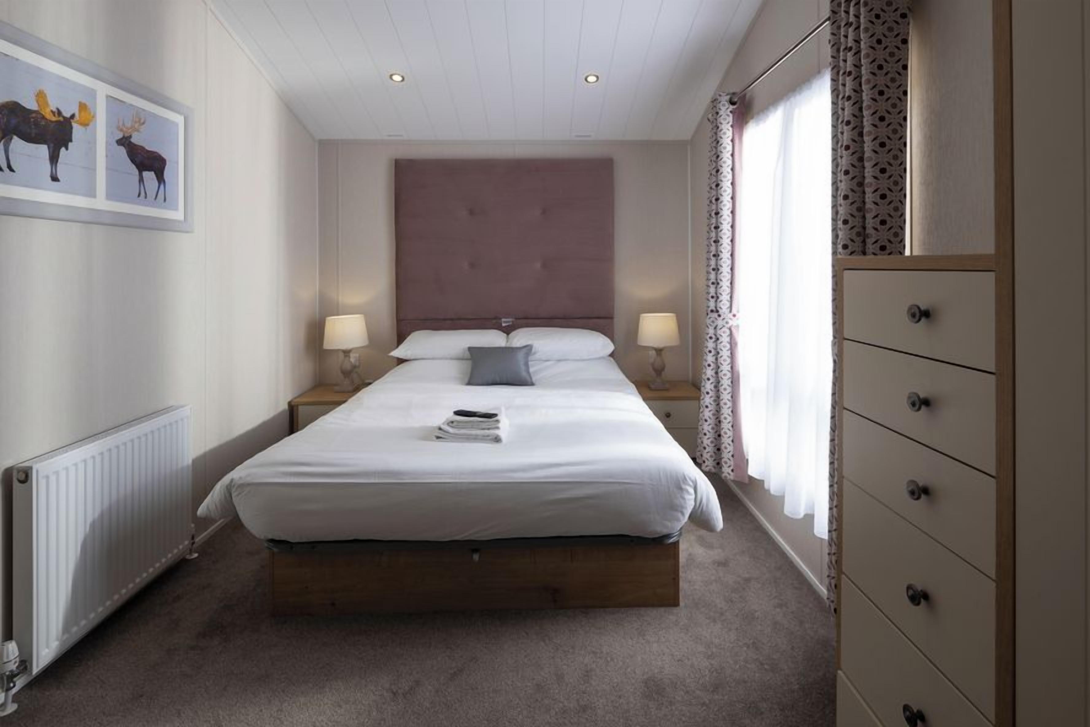 A bedroom with a large bed, bedside lamps, a dresser, and a framed picture on the wall.
