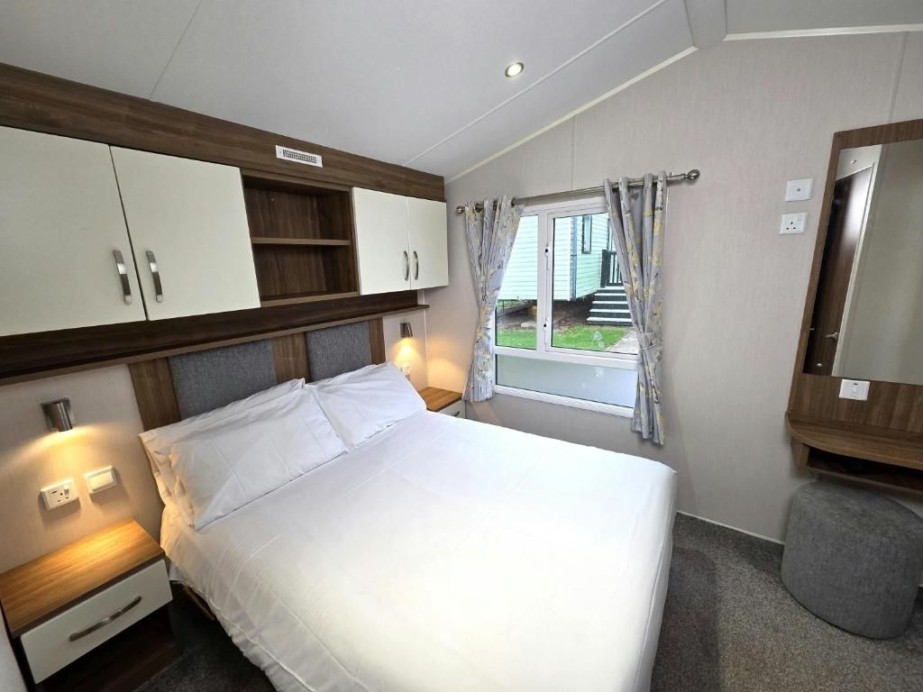Quarto de hotel com cama, mesas de cabeceira, guarda-roupa, janela com cortinas e um banquinho.