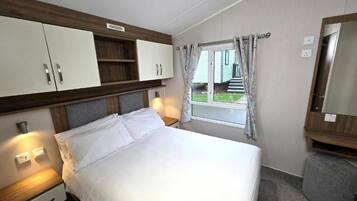 Quarto de hotel com cama, mesas de cabeceira, guarda-roupa, janela com cortinas e um banquinho.
