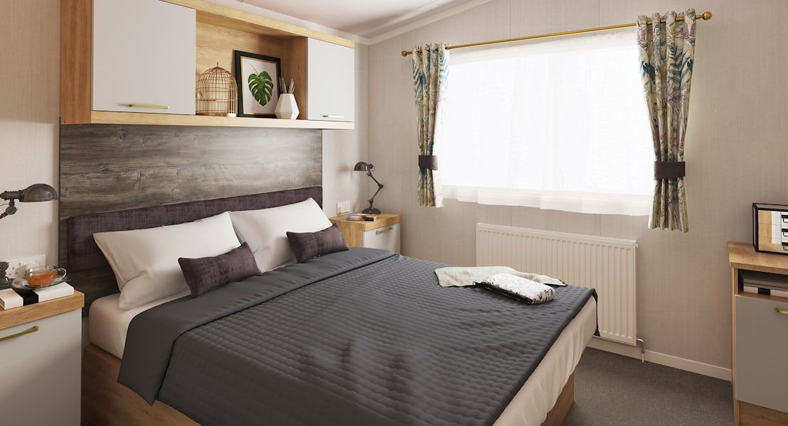 A bedroom with a bed, bedside tables, a nightstand, a window with curtains, and a radiator.