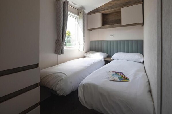 A small, compact room with two single beds, a window with curtains, and a built-in cabinet above the beds.