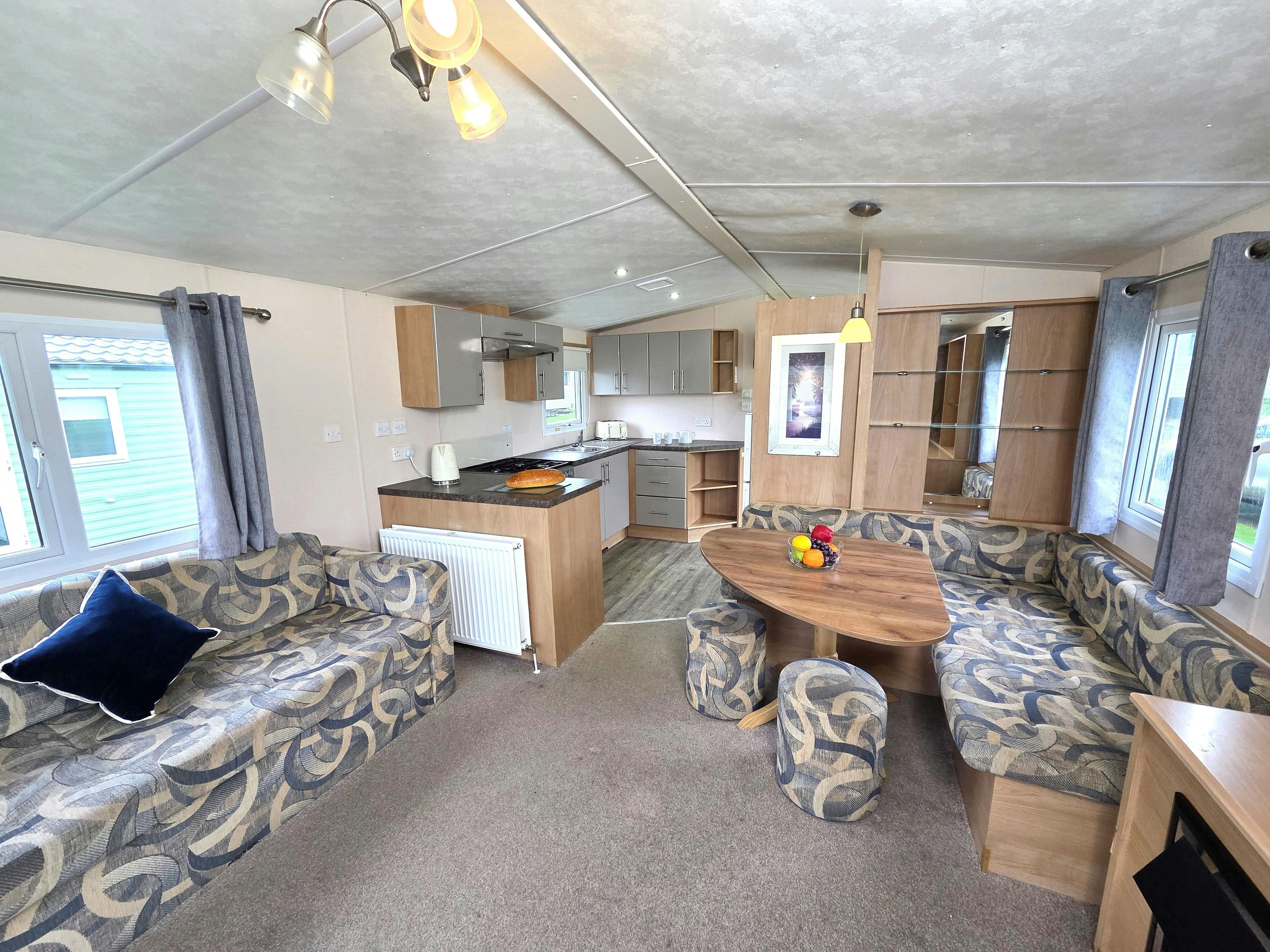 A compact RV interior with a kitchenette, seating area, and a dining table.