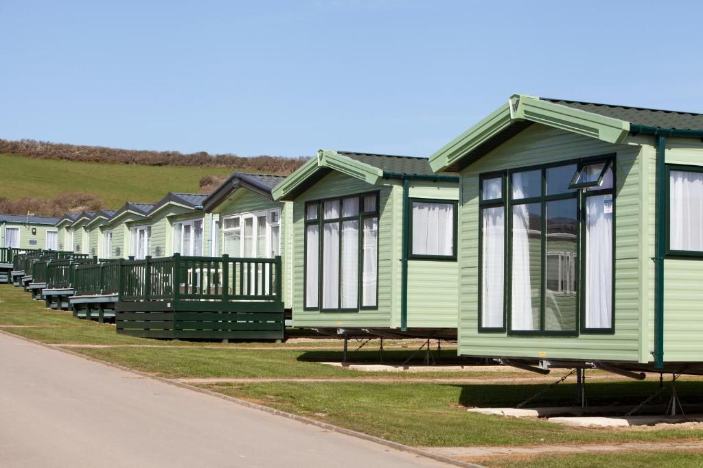 A row of green mobile homes with white windows and green trim, aligned along a paved road.