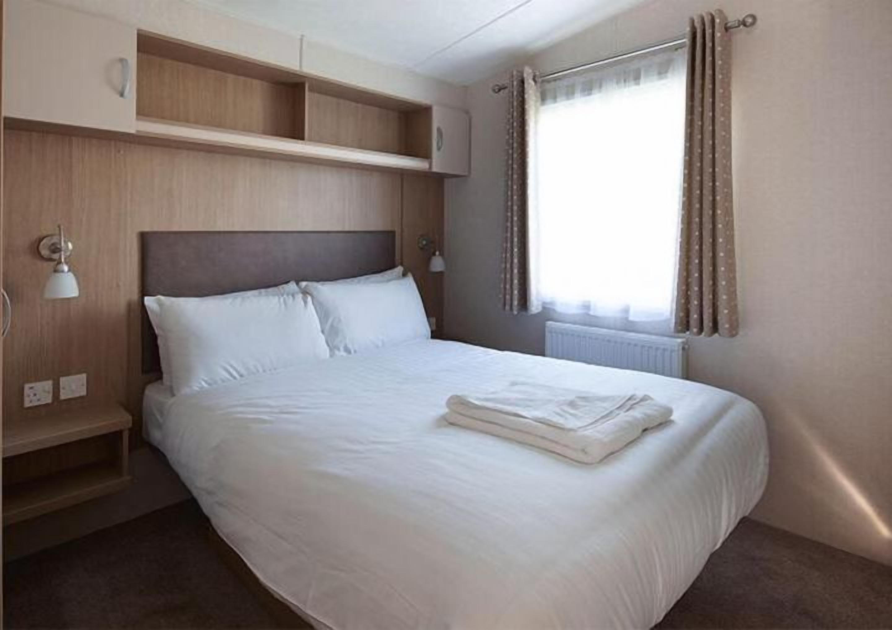 A single bed with a headboard, a bedside table with a lamp, and a window with curtains.