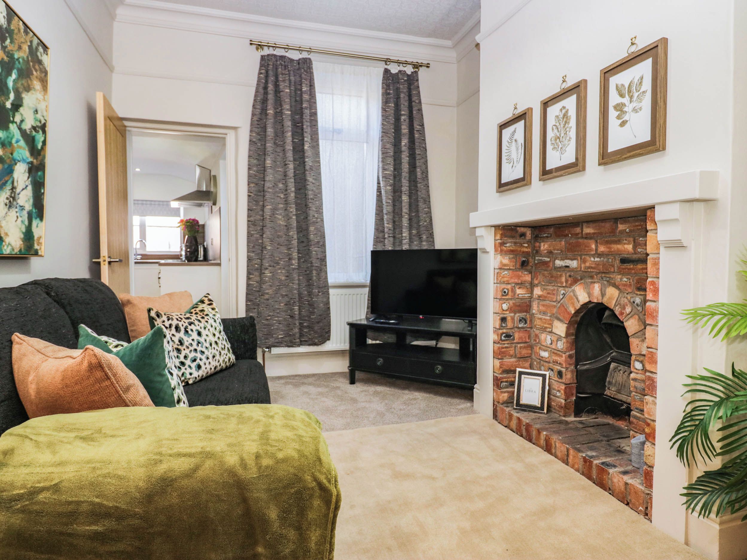 A living room with a sofa, television, fireplace, and framed botanical prints.