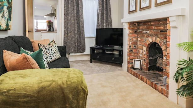 A living room with a sofa, television, fireplace, and framed botanical prints. - Cumbria Townhouse (Workington)