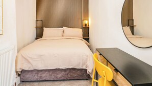A bedroom with a bed, bedside table, chair, and a large mirror. - Cumbria Townhouse (Workington)
