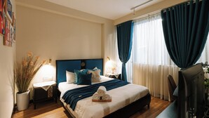 Ein Hotelzimmer mit Bett, Nachttischen, einem Schreibtisch und Vorhängen.