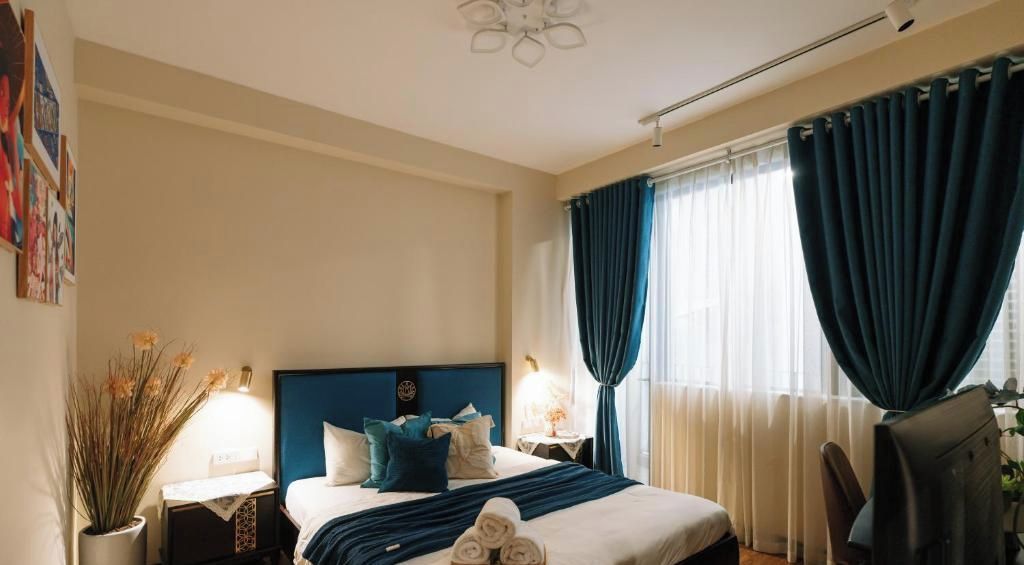 A hotel room with a bed, a nightstand, a lamp, a chair, and curtains.