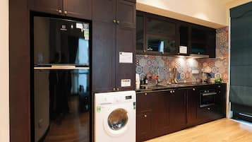 Een praktische keuken met donkerhouten kastjes, een ingebouwde wasmachine, een koelkast en een betegelde spatwand.