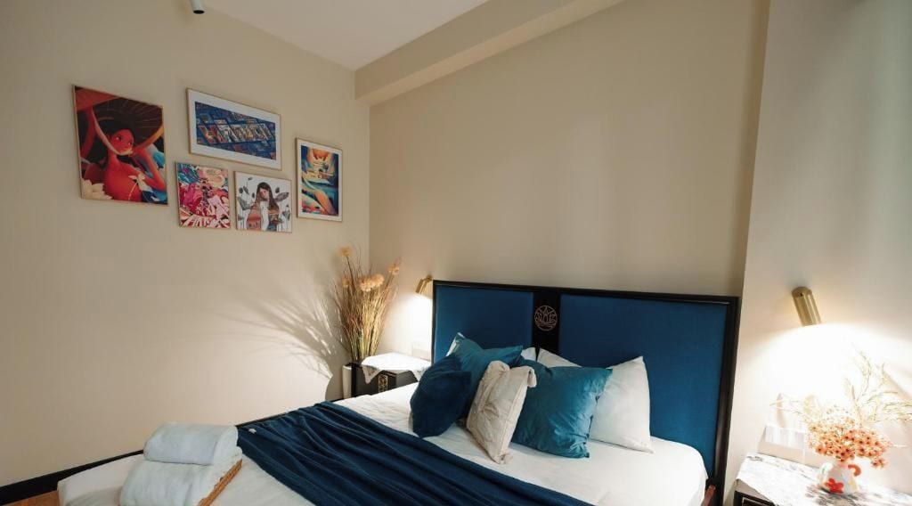 A hotel room with a bed, wall art, and a nightstand with a lamp.