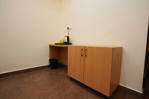 Una habitación con un armario de madera, un cubo de basura y una tetera en un estante.