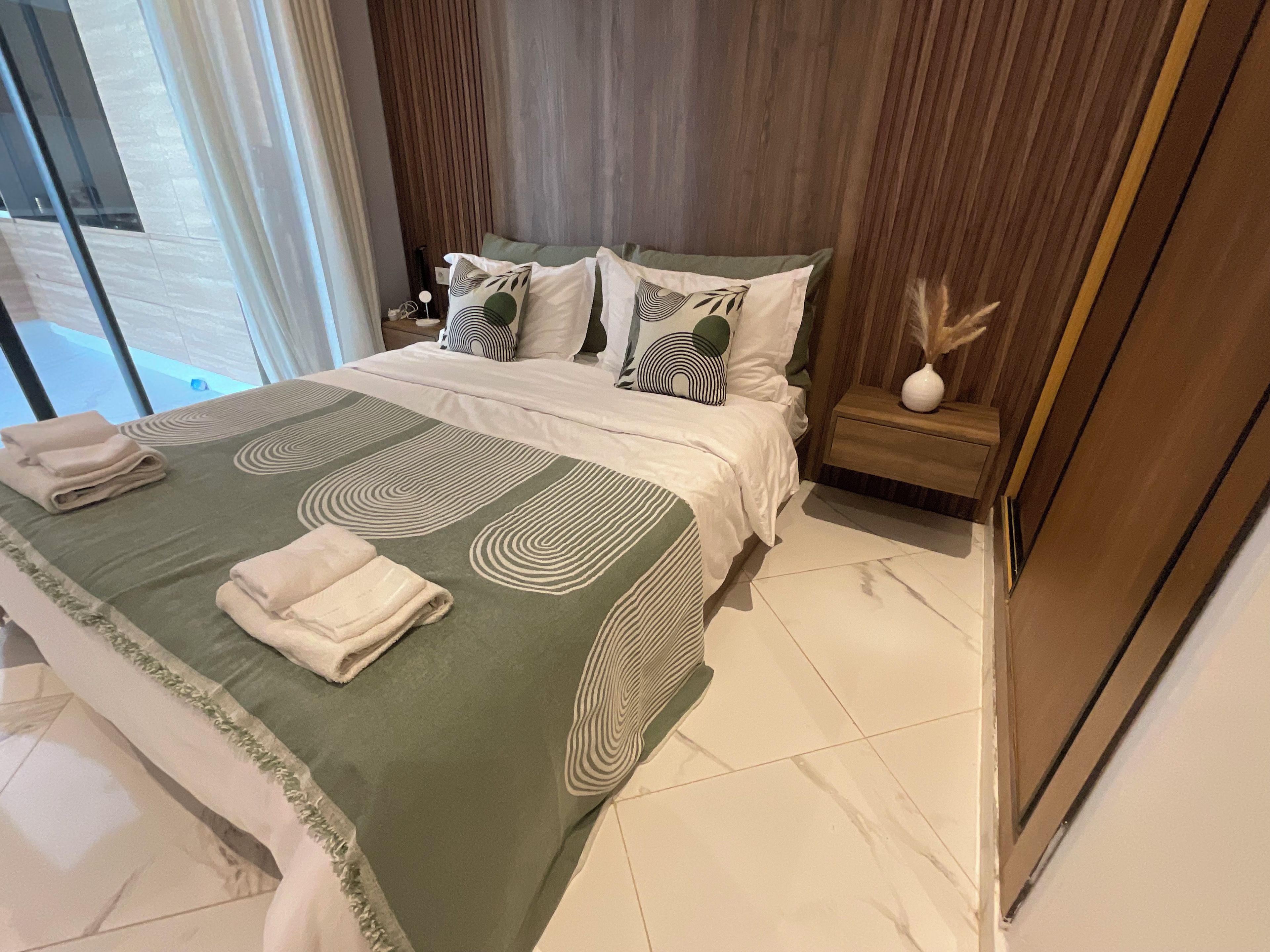 A modern bedroom with a large bed, a nightstand, and a view of the outside.