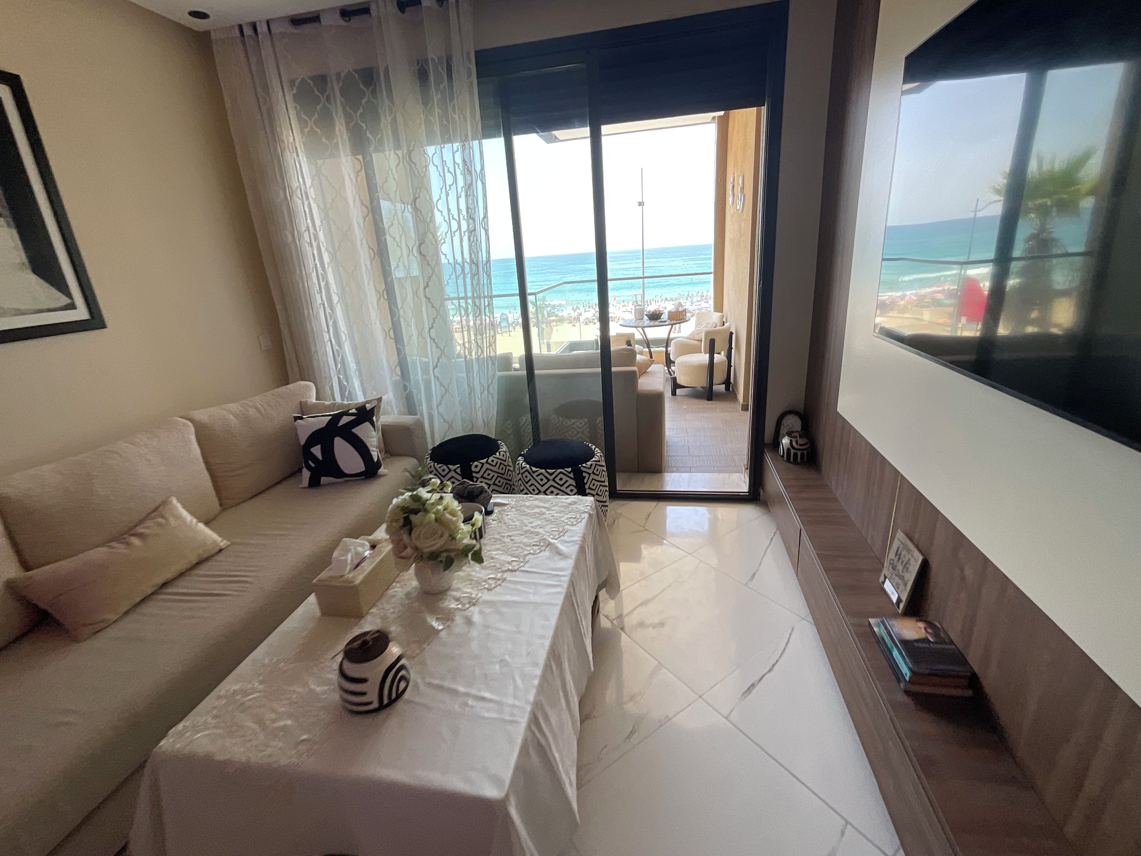 A living room with a sofa, a coffee table with decorative items, and a view of the beach through a glass door.
