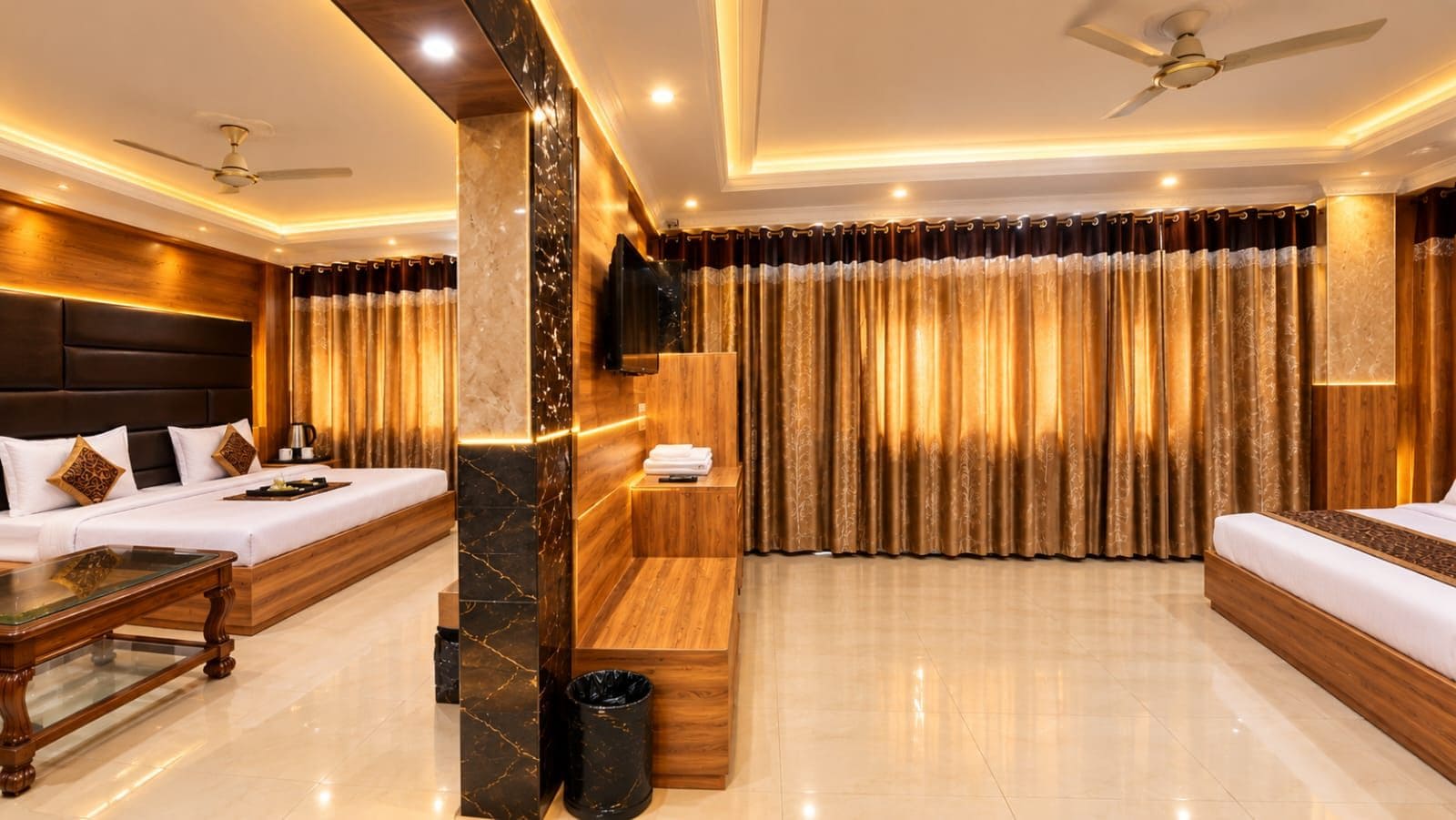 A hotel room with a sofa, a bed, a coffee table, a TV, and a large window with curtains.