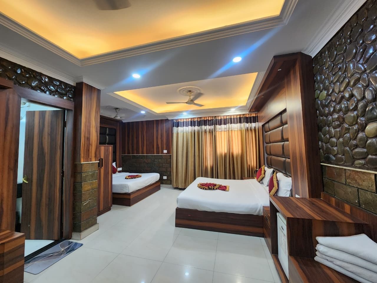 A hotel room with two beds, a ceiling fan, and a stone wall.
