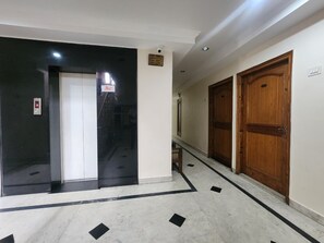 A hallway with a black elevator, wooden doors, and a tiled floor with black accents. - Shanker Palace Near Main Market Katra (Reasi)