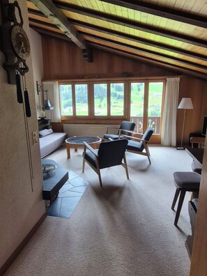 Ein gemütliches Zimmer mit einer Couch, Stühlen, einem Tisch und Blick durch große Fenster.