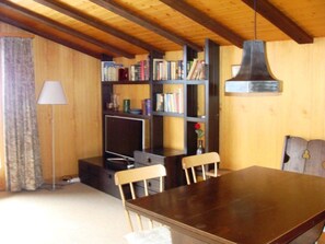 Ein Holzinnenraum mit Esstisch, Stühlen, einem Bücherregal und einer Lampe.