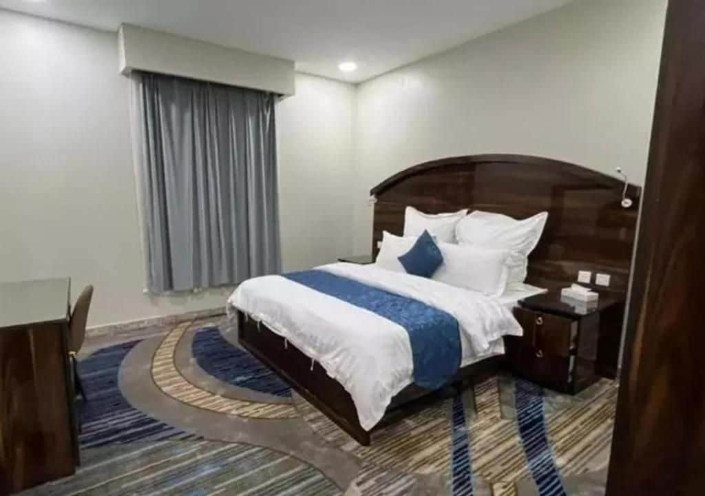 Una habitación de hotel con una cama, una mesita de noche, un escritorio y una ventana con cortinas.