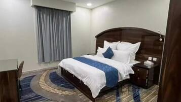 Una habitación de hotel con una cama, una mesita de noche, un escritorio y una ventana con cortinas.
