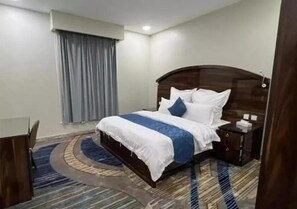 A hotel room with a bed, a nightstand, a desk, and a window with curtains. - Elaf Al Sharqyah Al Aziziah Hotel  (Al Khobar)