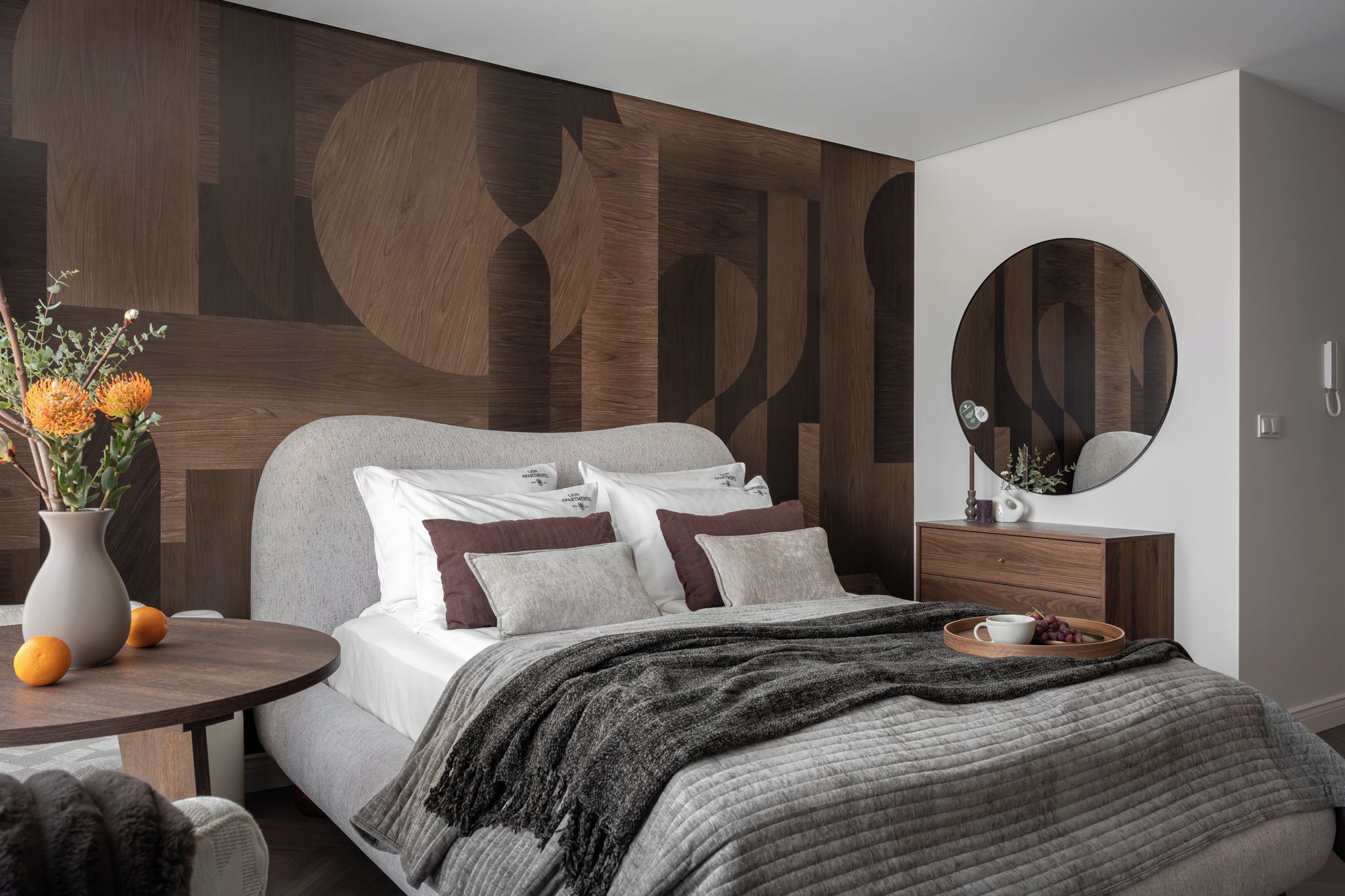 Quarto moderno com cama, mesa de cabeceira e espelho redondo.