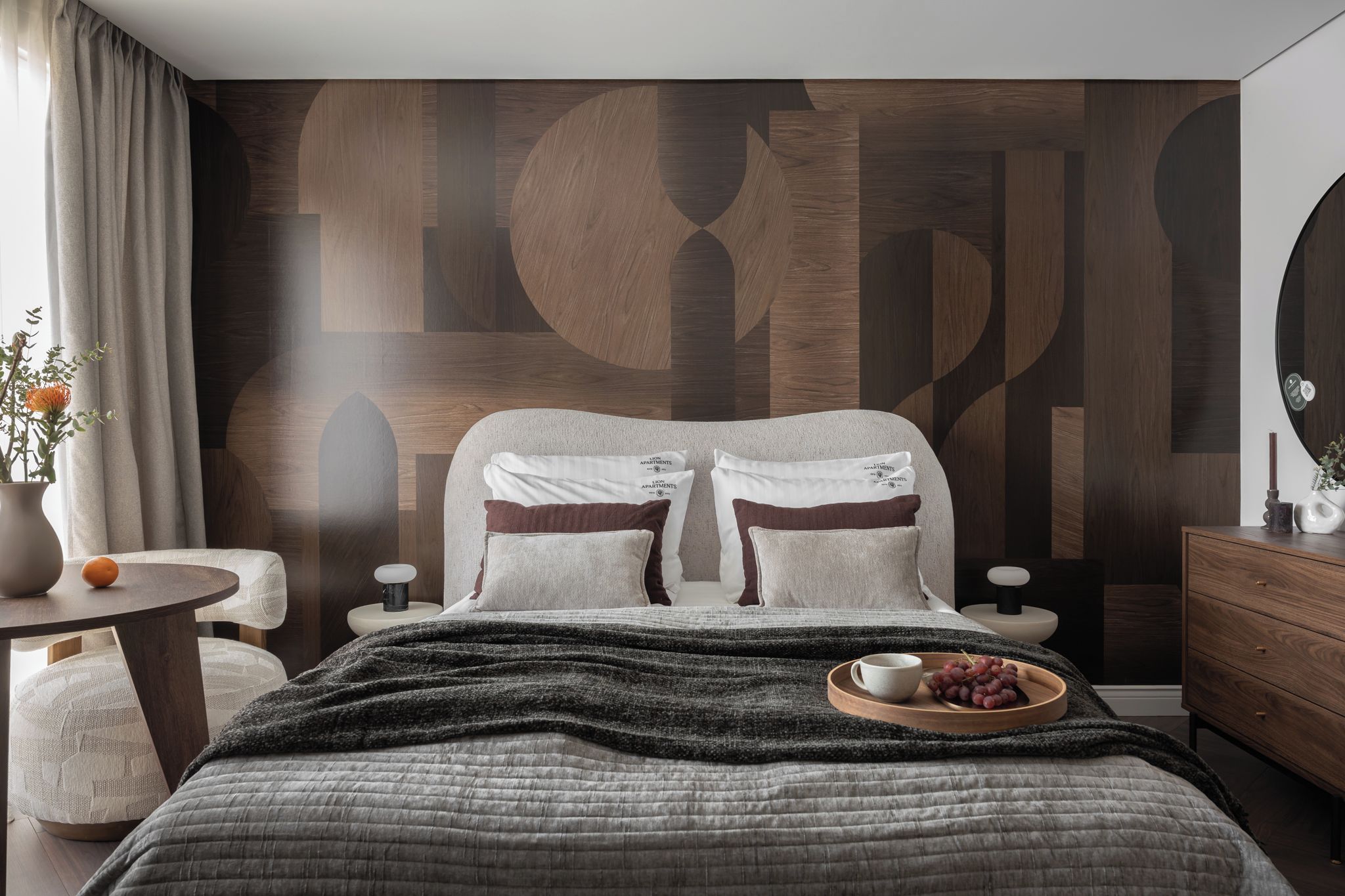 A modern bedroom with a large bed, a bedside table, a small round table, and a dresser.