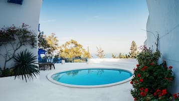 Una piscina con vistas al mar, rodeada de muros blancos y algo de vegetación.