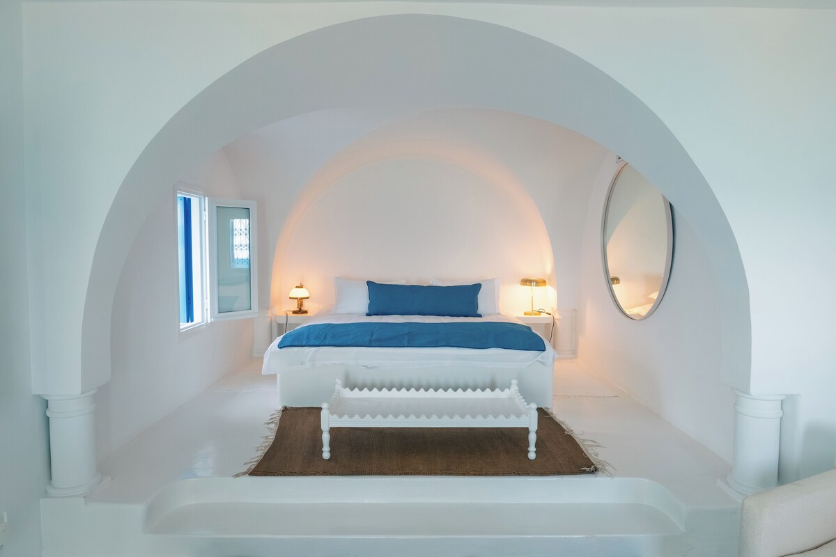 Un dormitorio con una cama blanca, un cojín azul decorativo y un espejo grande en la pared.