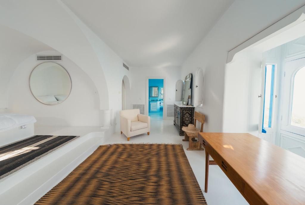 A modern hotel room with a bed, a round mirror, a sofa, a wooden table, and a patterned rug.