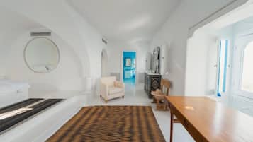 A modern hotel room with a bed, a round mirror, a sofa, a wooden table, and a patterned rug.