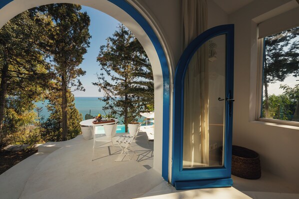 Una habitación con vista al mar, una mesa blanca con sillas y una puerta azul.