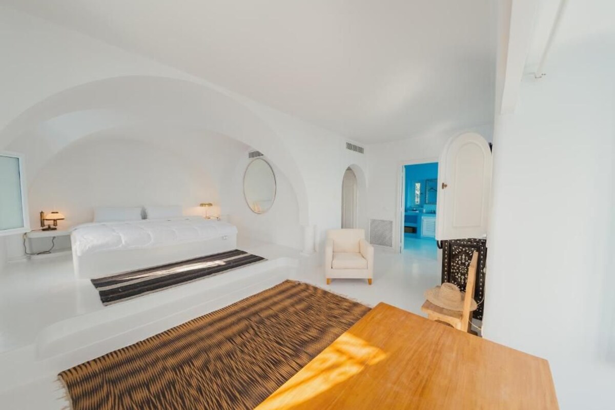 Une chambre à coucher moderne et minimaliste, avec un grand lit, une table en bois et une vue sur la mer.