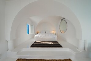 Un dormitorio con una cama blanca, un tapete a rayas negras y blancas, una bañera blanca y un espejo grande en la pared.