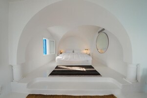 Un dormitorio con una cama blanca, un tapete a rayas negras y blancas, una bañera blanca y un espejo grande en la pared.