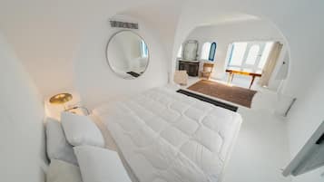 Un dormitorio con una cama grande, un espejo redondo, una mesita de noche y vistas a un comedor a través de un ventanal en arco.