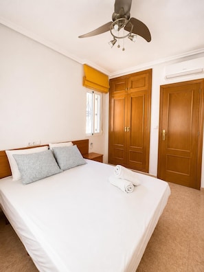 Ein Hotelzimmer mit einem Bett, einem Deckenventilator, Holzschränken, einem Fenster mit gelben Vorhängen und einer Klimaanlage.
