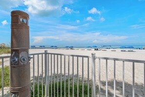 Una spiaggia con una recinzione bianca, un pilastro di pietra e ombrelloni blu.
