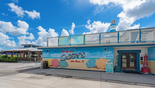 Un edificio con un mural alusivo a la playa, un letrero que dice 'Greetings from CADDY'S' y una entrada visible.