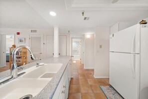 A kitchen with a double sink, a refrigerator, and a tiled backsplash. - New Direct Beachfront 3/2 Upscale, Beachfront Condo, Recliners, Pool, Hot Tub (Indian Rocks Beach)